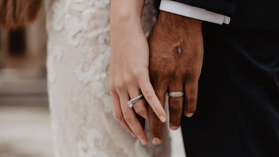 a bride and groom touch hands during their wedding while wearing their rings