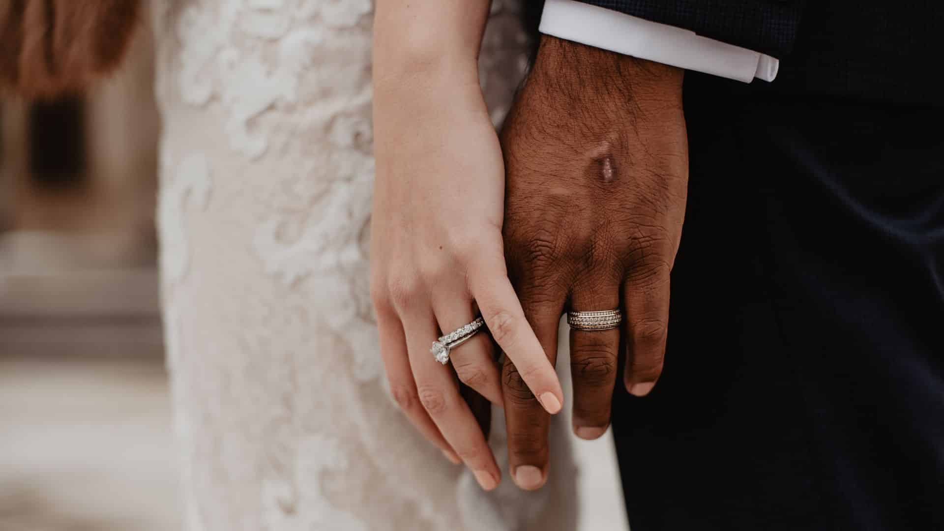 a bride and groom touch hands during their wedding while wearing their rings