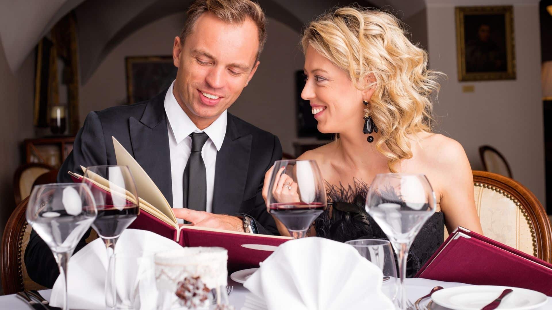 a couple is drinking wine and ordering off the menu at a fine dining establishment