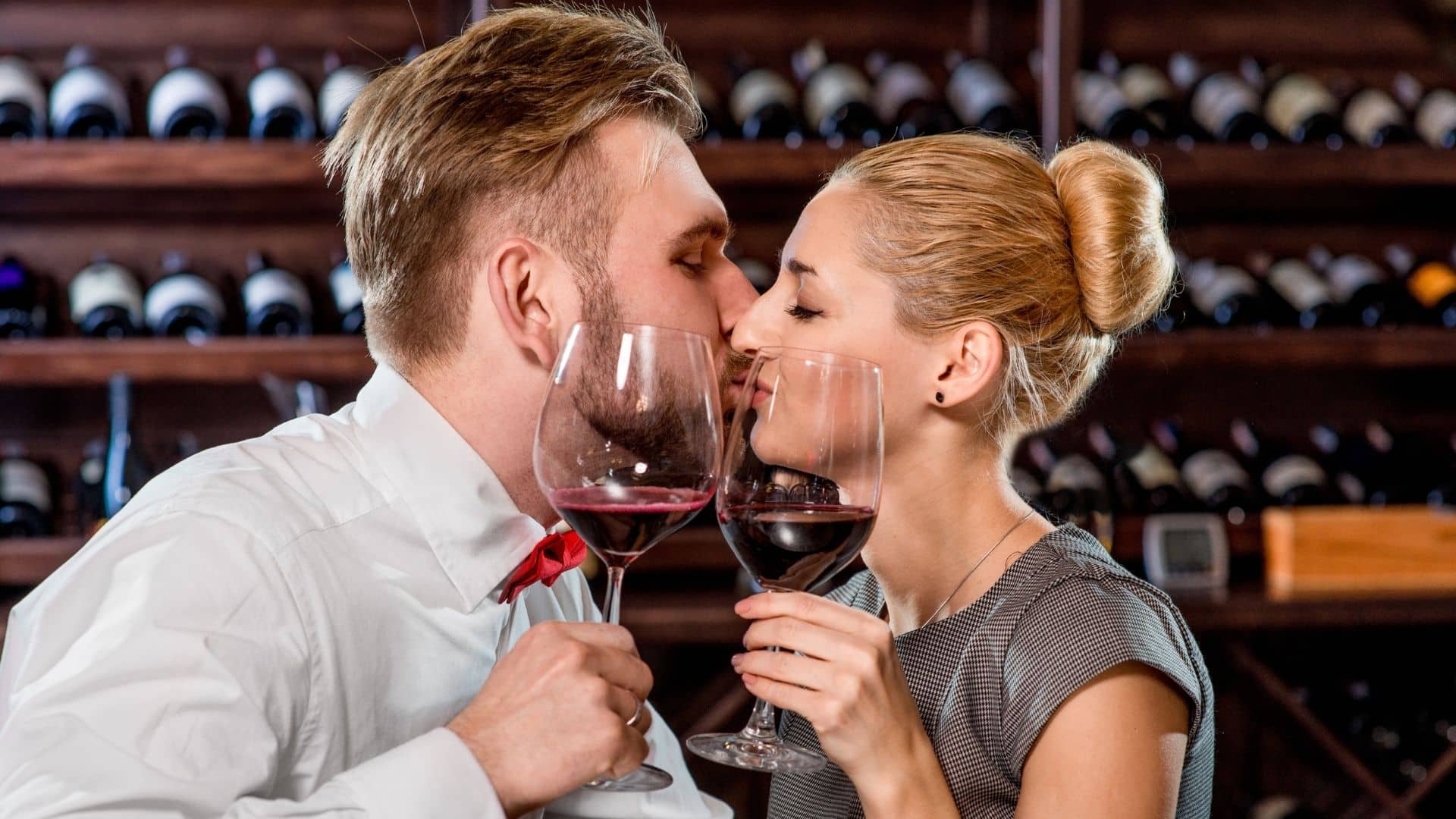 man and woman kissing while holding glasses of wine at a wine tasting