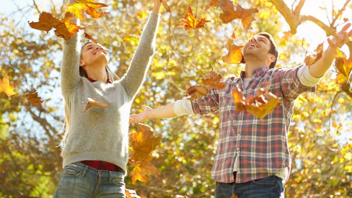 a couple throws leaves up into the air at a park on a fall day