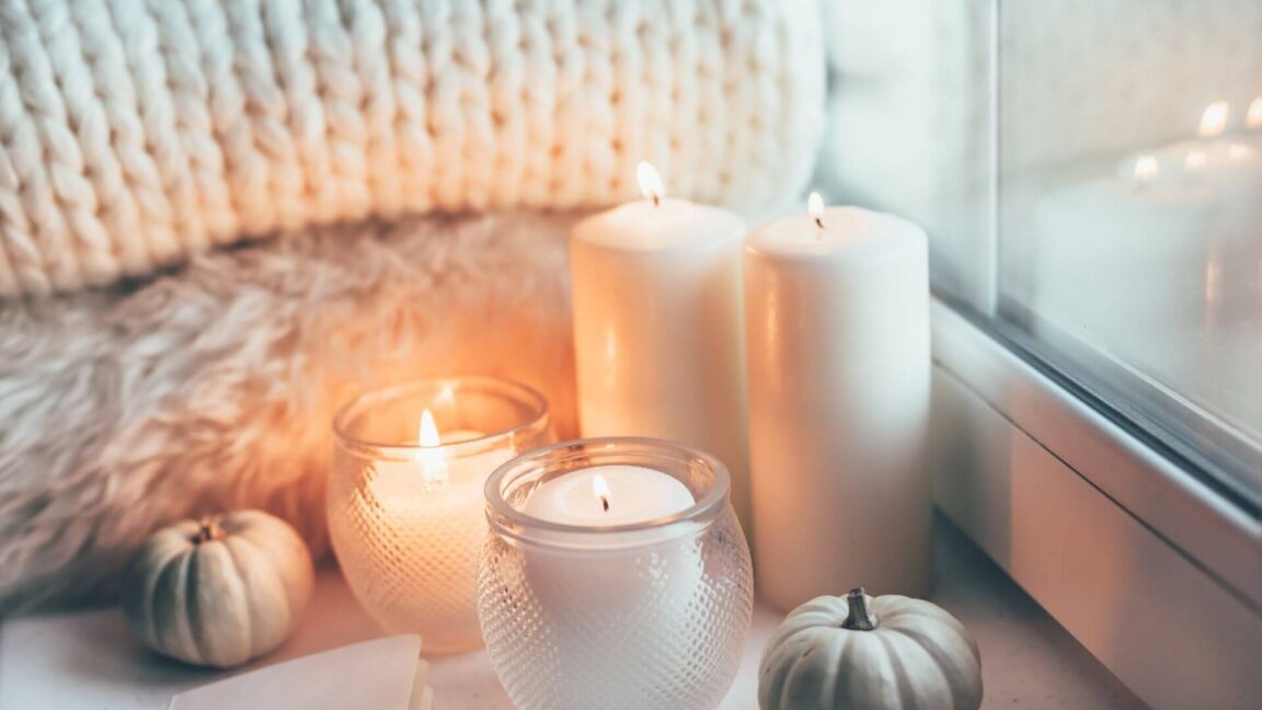 folded soft blankets, several glowing candles nestled against a window with snow outside