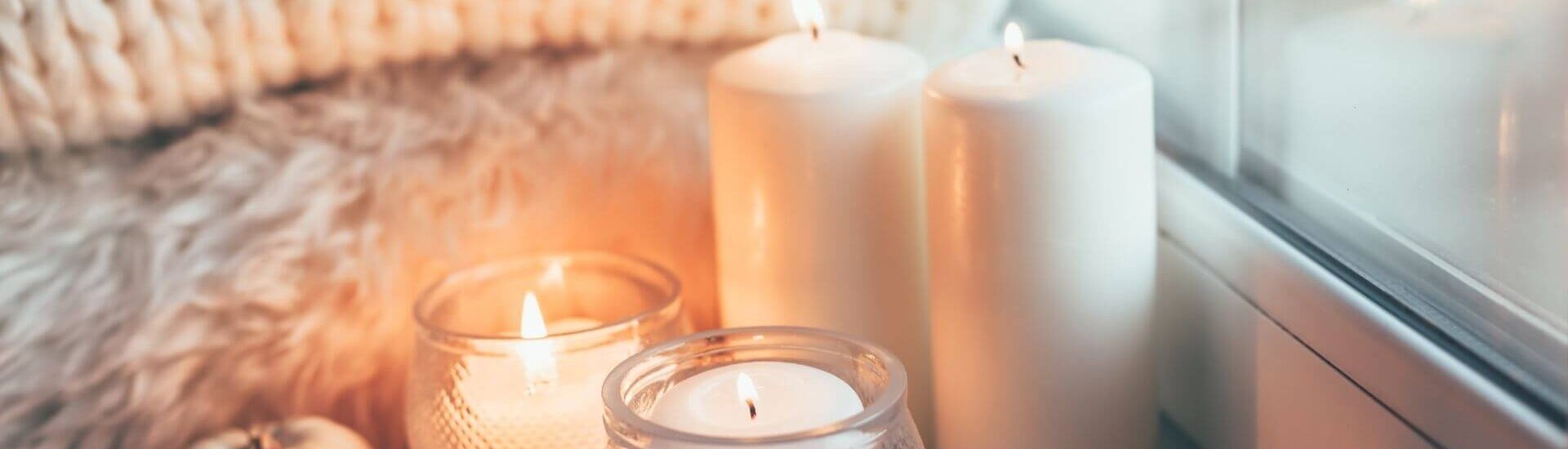 folded soft blankets, several glowing candles nestled against a window with snow outside