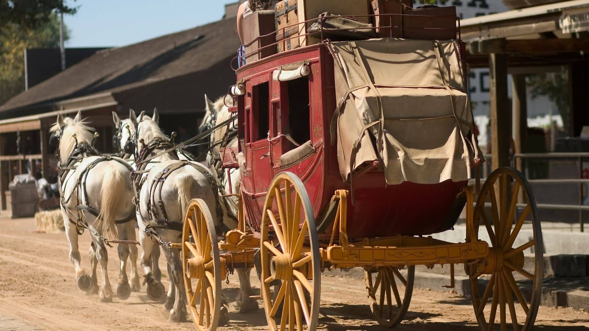 a four-horse-drawn carriage going down a dusty street with trunks on top of the red carriage