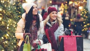 two ladies dressed warm holding shopping bags on a street decorated for the holidays